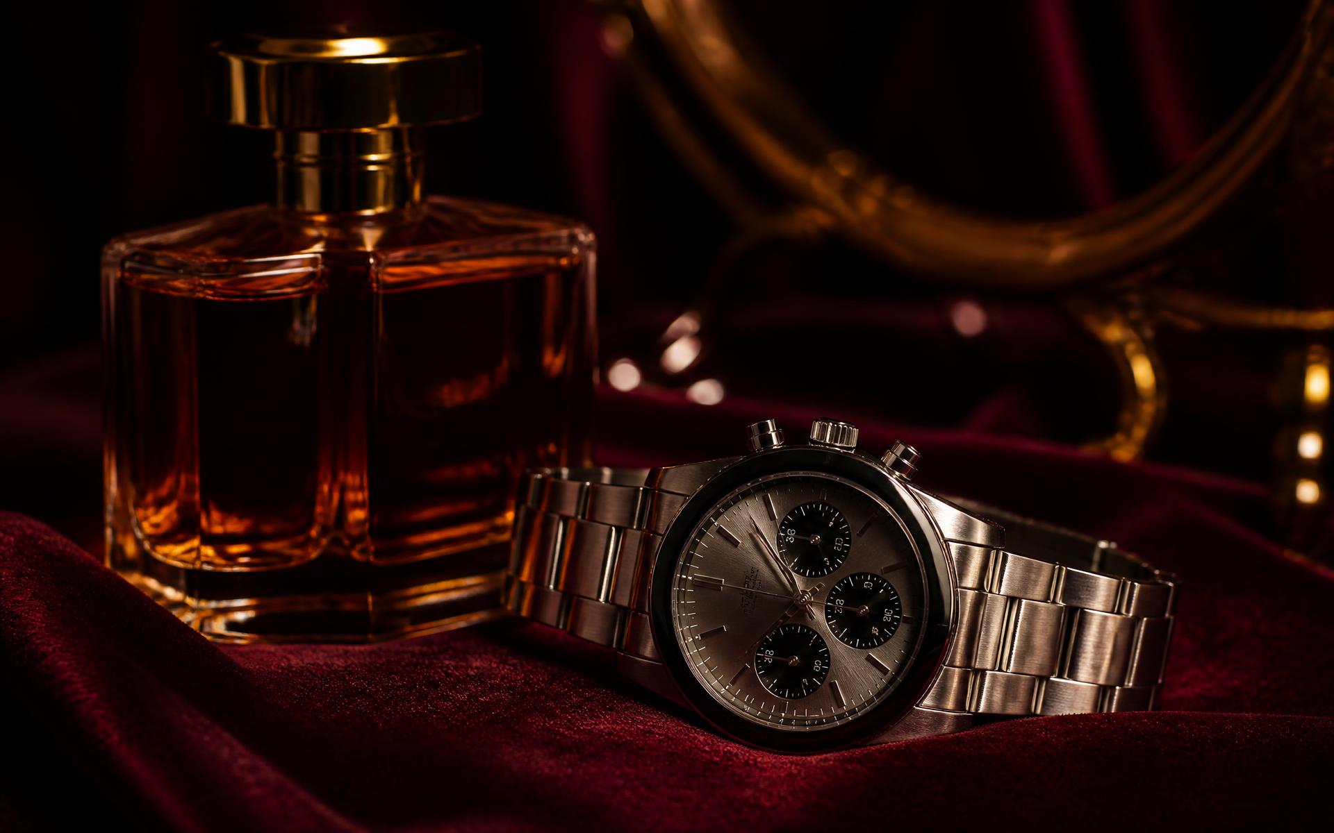 Reloj de lujo y frasco de perfume sobre superficie oscura